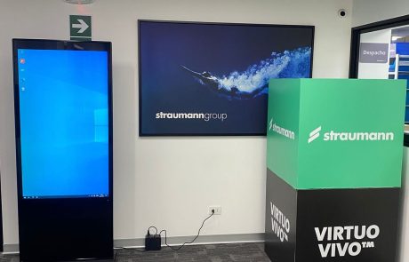 Tótem digital vertical junto a pantalla en stand de congreso